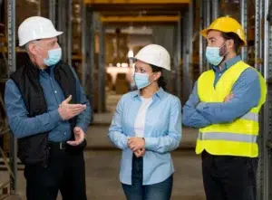 Team members wearing hard hats and masks engage in a safety talk, reflecting the need for open dialogue on hidden workplace risks.
