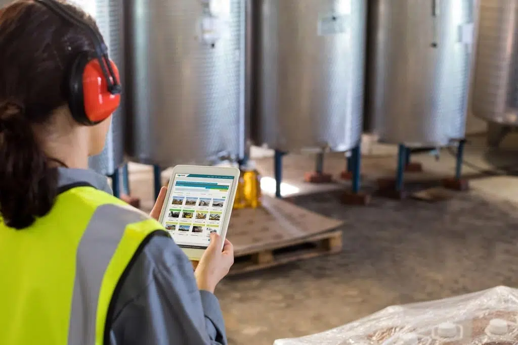 A construction worker in a safety vest and hard hat using a tablet in a warehouse.
