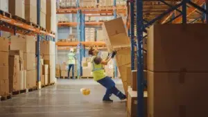 Worker reacts to falling boxes in a warehouse, showcasing the importance of hazard ID tools in promoting safer worksites.