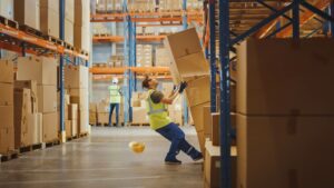 Worker reacts to falling boxes in a warehouse, showcasing the importance of hazard ID tools in promoting safer worksites.