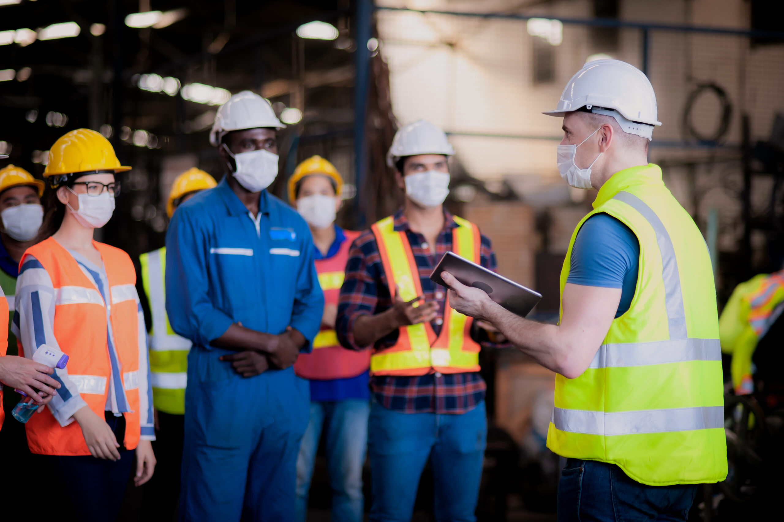 Foreman holding tablet during digital toolbox talk with workers in a factory.