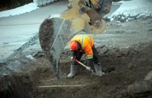 Workers in safety vests excavating ground with shovels at a construction site.