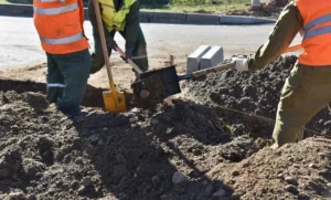 Workers in safety vests excavating ground with shovels at a construction site.