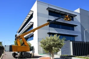 Boom lift raising worker for structural installation, emphasizing safe high-access operation​.