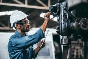 Technicians in hard hat inspect machinery while recording findings on a tablet.