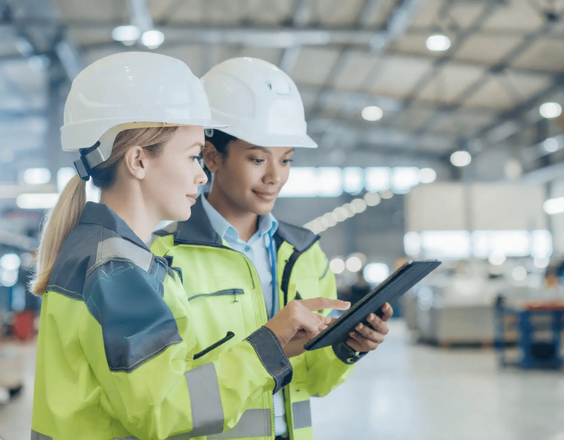 Two workers in PPE checking competency status and approvals on a tablet in a factory.