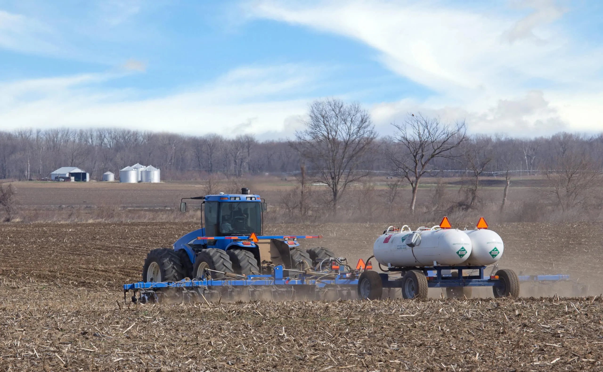Farm tractor pulling twin NH₃ nurse tanks during field application, showing agricultural use of anhydrous ammonia.