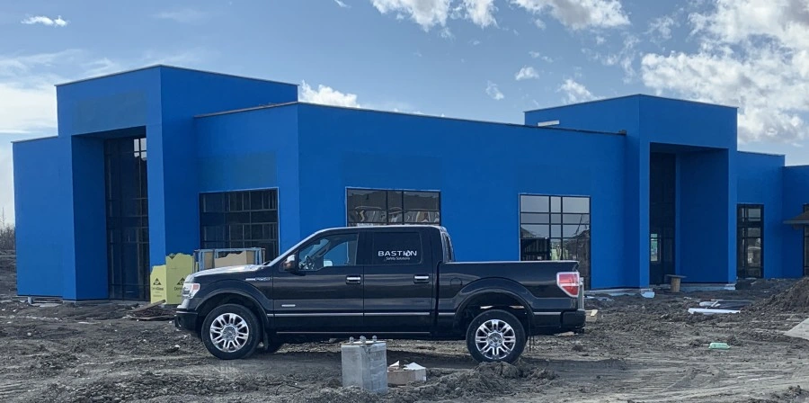 Bastion safety truck on site. A large blue building lies behind a Bastion truck with a bastion insignia. A sunny blue sky with sparse cloud coverage frames the whole image.