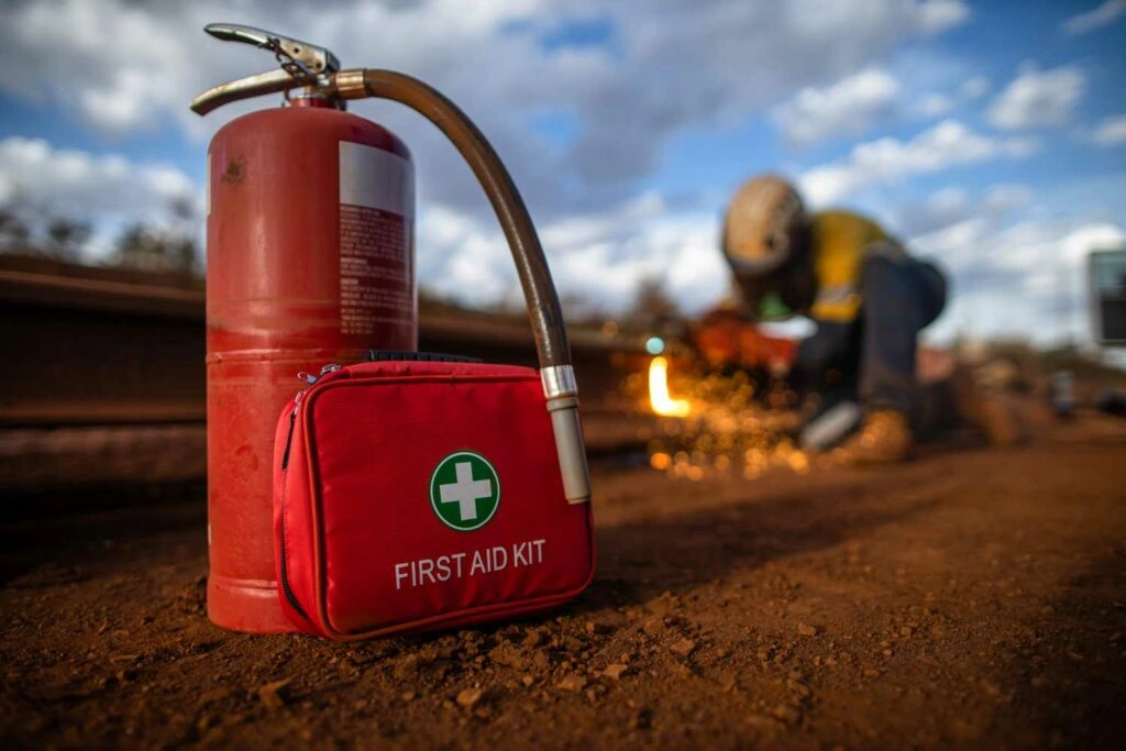 Fire Safety Equipment in focus while a worker performs hot work on a rail with a grinder. A good example of fire safety prep for a workplace safety topic discussion.